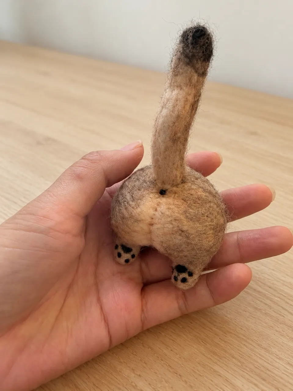 A needle-felted tabby cat rear-half sculpture: rump, upright tail and hind paws only, with no head or front half.
