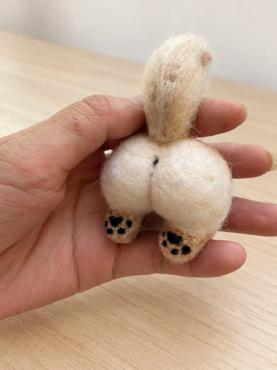 A needle-felted cream cat rear-half sculpture: rump, tail and hind paws only, with no head or front half.